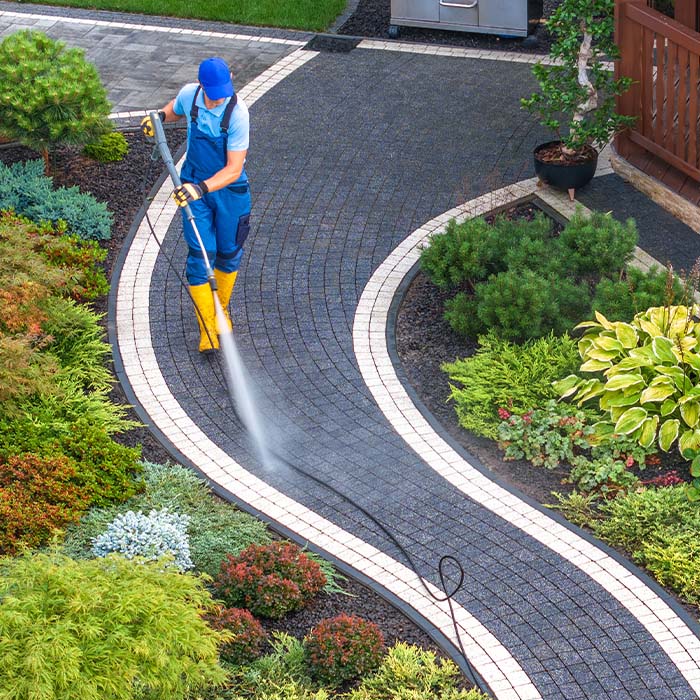 Homeowner cleaning backyard garden brick paths using pressure washer